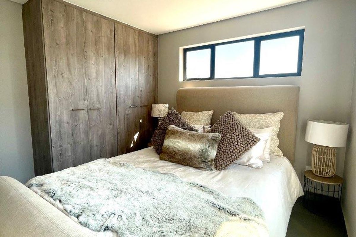 A well-maintained bedroom featuring built-in wooden cupboards, modern recessed ceiling lighting, and a horizontal window providing natural light.