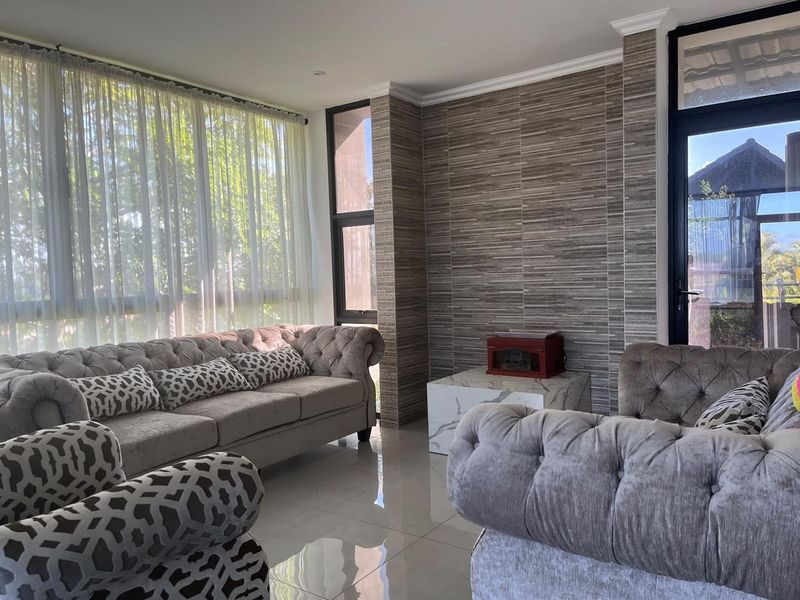 A bright living room featuring large windows, polished tiled flooring, and a modern textured feature wall with crown molding details.