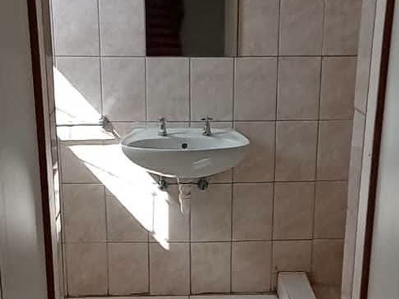 A compact, tiled bathroom featuring a wall-mounted basin and a recessed mirror, presenting a functional space in need of cosmetic updates.