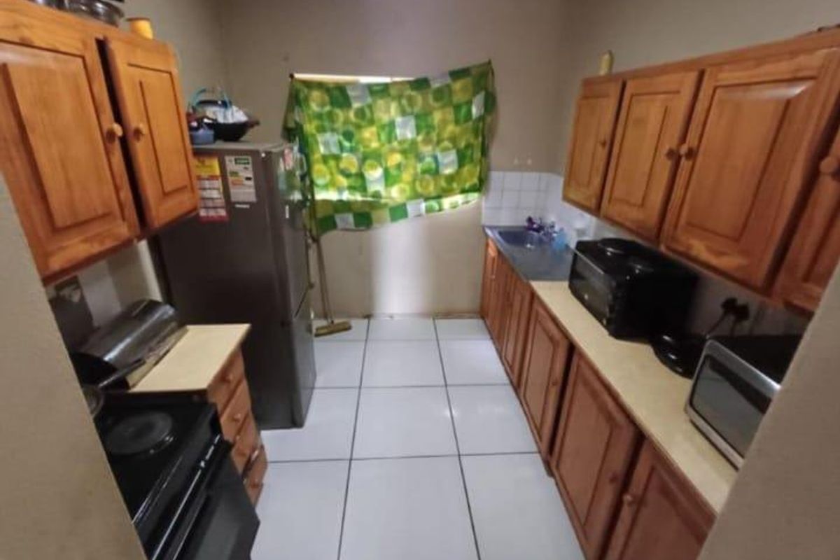 A compact galley-style kitchen featuring wooden cabinetry, tiled flooring, and a functional layout with built-in stove and sink area.