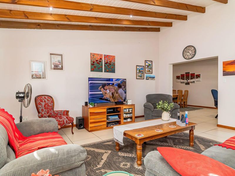 Spacious living room featuring exposed timber ceiling beams, tiled flooring, and recessed lighting, with an open-plan flow into the adjacent dining area.