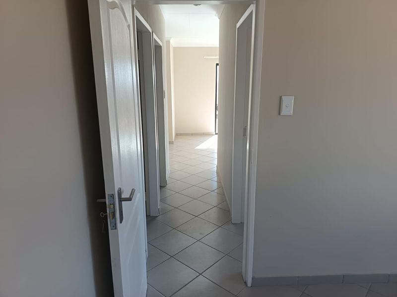 A clean, empty hallway featuring neutral wall tones and tiled flooring, providing access to multiple rooms within the home.