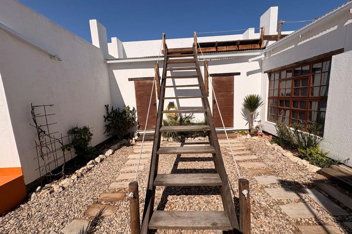 A rear courtyard featuring a central wooden staircase leading to an upper level, surrounded by gravel landscaping and white exterior walls.