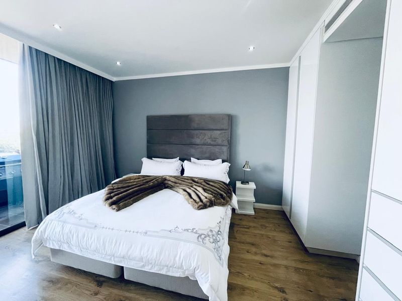 Modern bedroom featuring laminate flooring, built-in cupboards, recessed lighting, and direct access to a private balcony through sliding glass doors.