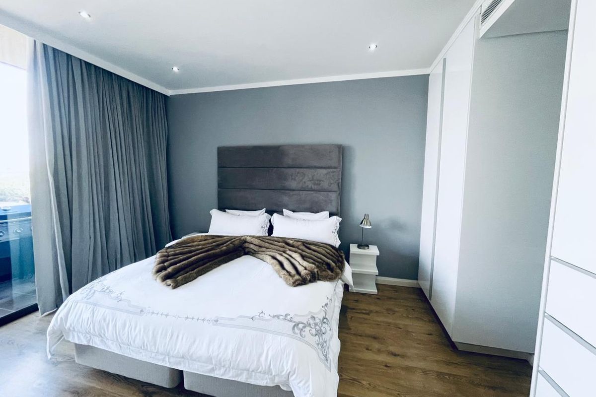 Modern bedroom featuring laminate flooring, built-in cupboards, recessed lighting, and direct access to a private balcony through sliding glass doors.
