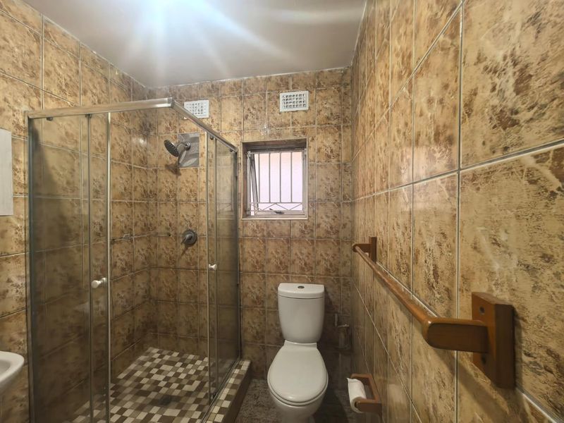 A functional bathroom featuring a glass-enclosed shower, toilet, and full-height wall tiling. The space is ready for a modern update.