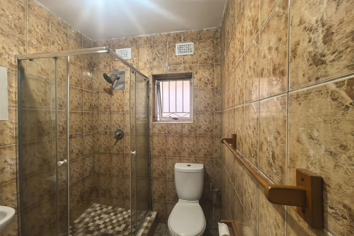 A functional bathroom featuring a glass-enclosed shower, toilet, and full-height wall tiling. The space is ready for a modern update.