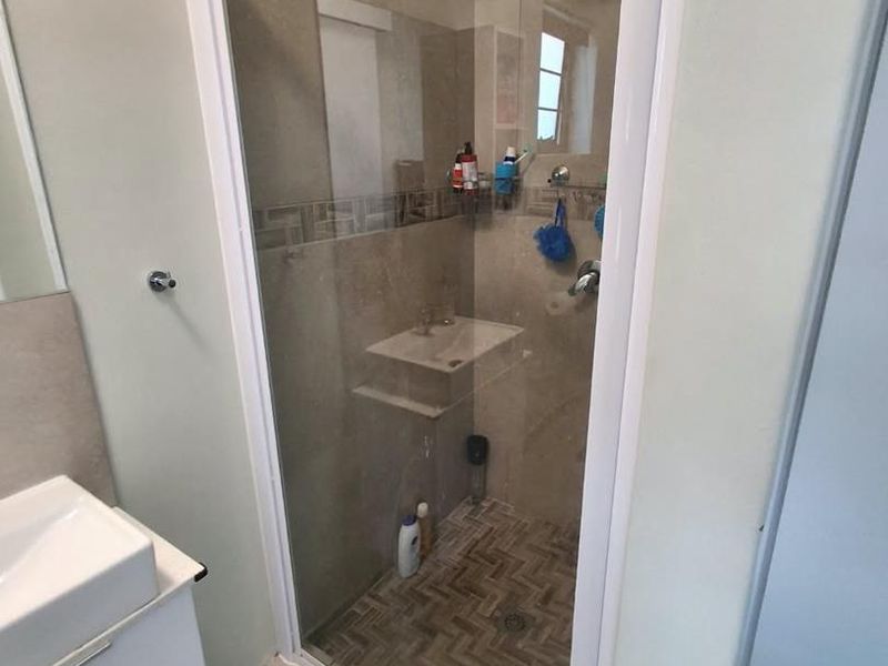 A modern bathroom featuring a tiled shower enclosure with a rain shower head and a sleek vanity basin with storage cabinet.