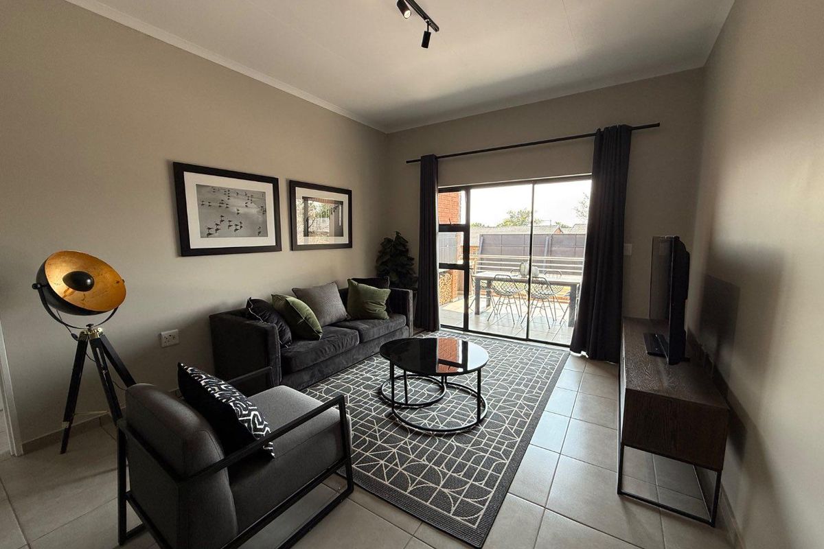 A well-maintained living room featuring tiled flooring, track lighting, and large sliding glass doors providing direct access to an outdoor patio area.