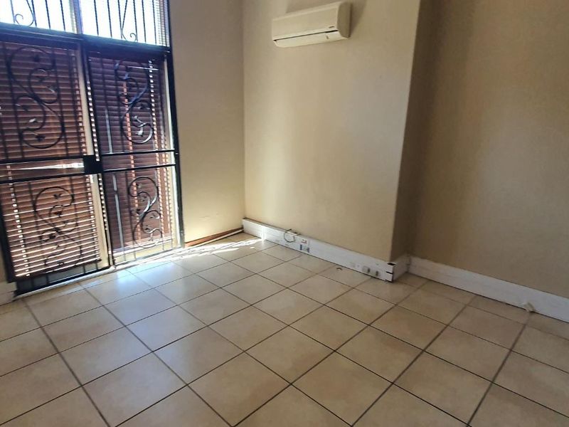 An empty office space featuring tiled flooring, a wall-mounted air conditioning unit, and a secure metal entrance gate.