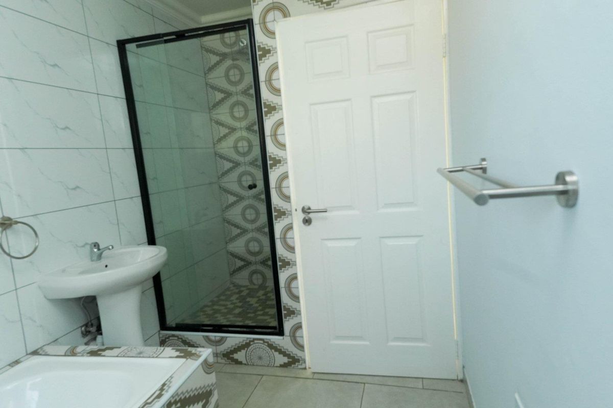 A modern bathroom featuring a glass-enclosed shower with patterned tile accents, a pedestal sink, and a towel rail.