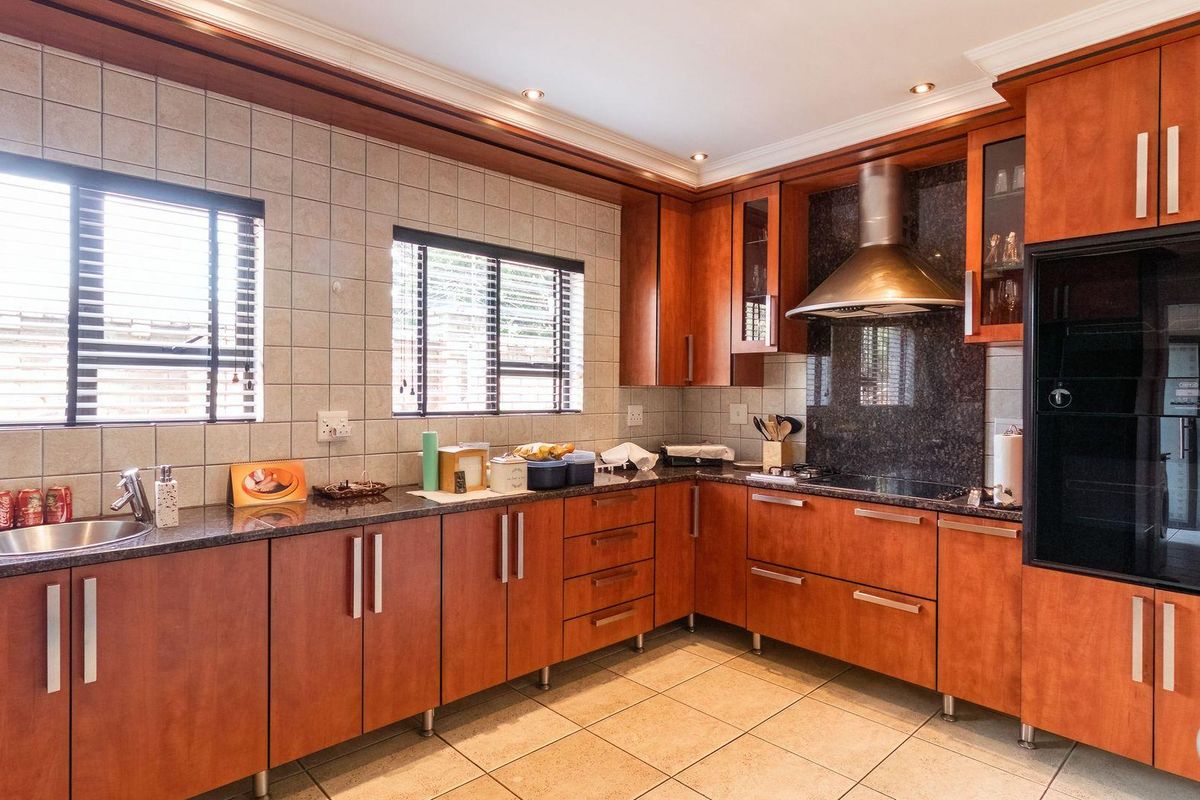 A well-maintained kitchen featuring warm-toned wooden cabinetry, granite countertops, tiled splashbacks, and integrated stainless steel appliances including a hob and extractor fan.