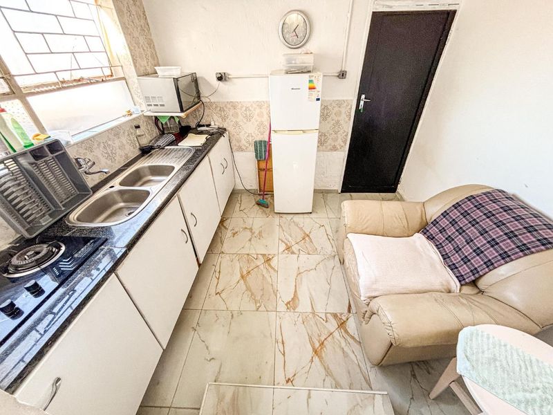 A compact kitchen featuring tiled flooring, granite countertops, a double basin sink, and built-in hob, requiring cosmetic updates to improve its overall condition.