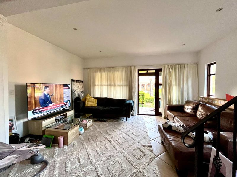 A spacious living room featuring tiled flooring, recessed lighting, and direct access to an outdoor patio area through a glass-paneled door.