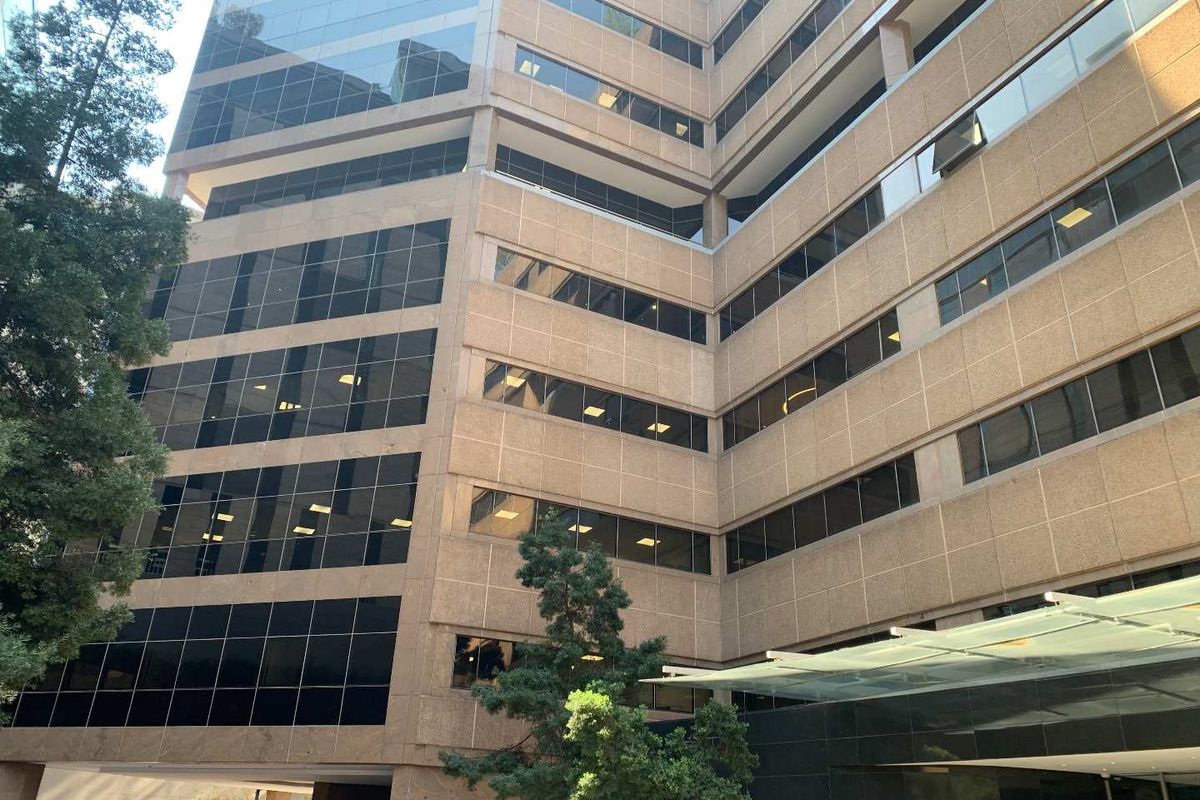 A modern multi-story office building featuring a glass curtain wall facade, tinted windows, and a prominent glass entrance canopy.