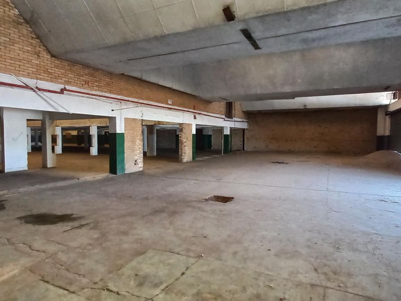Expansive industrial warehouse space featuring high vaulted ceilings, exposed brick walls, concrete flooring, and large roller shutter door access.