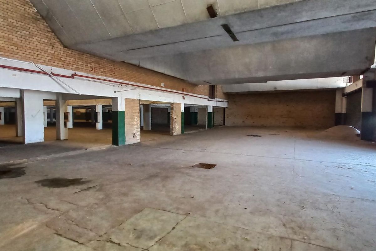 Expansive industrial warehouse space featuring high vaulted ceilings, exposed brick walls, concrete flooring, and large roller shutter door access.