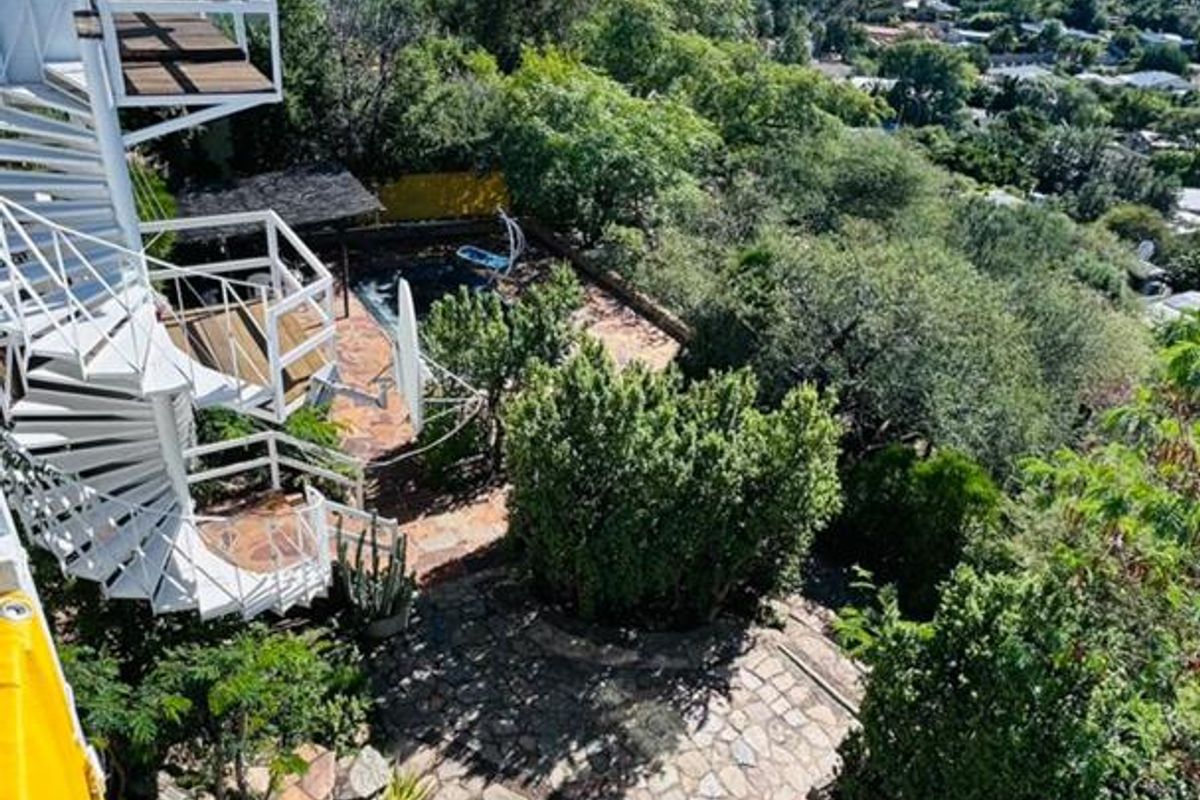 Elevated view of a multi-level garden featuring stone paving, a white spiral staircase, and lush hillside surroundings.