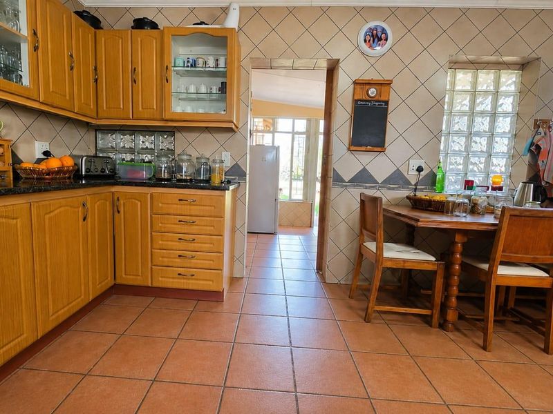 A functional kitchen featuring wooden cabinetry, granite countertops, and a distinctive glass block window, with tiled flooring and backsplash throughout.