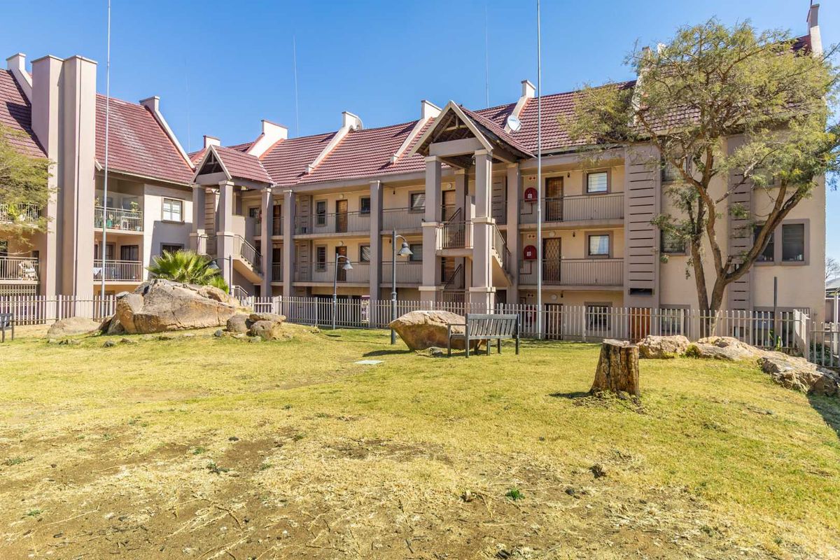 Exterior view of a multi-story apartment complex featuring a communal garden area with landscaped rocks and paved walkways.