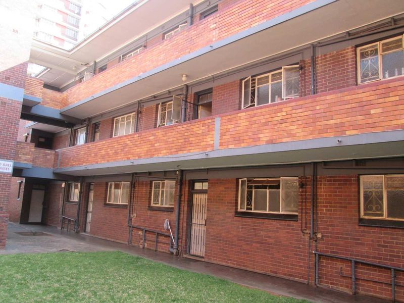 Exterior view of a multi-story apartment building featuring face brick construction, metal security gates, and shared concrete walkways.