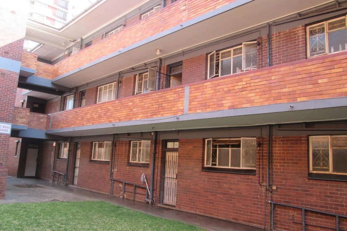 Exterior view of a multi-story apartment building featuring face brick construction, metal security gates, and shared concrete walkways.