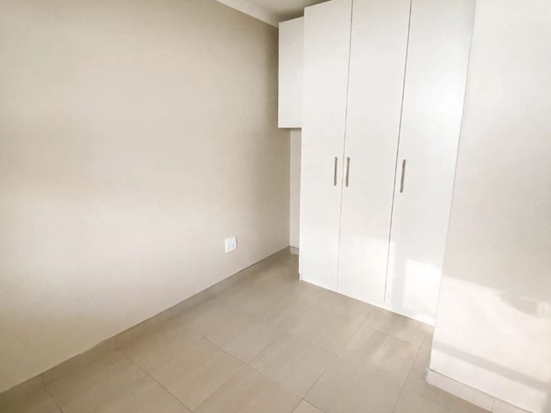 A clean, empty bedroom featuring neutral tiled flooring and white built-in cupboards, offering a blank canvas for personalization.