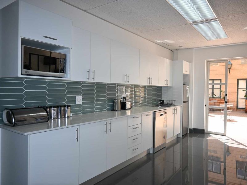 Modern office kitchen featuring white cabinetry, quartz countertops, a stylish tiled backsplash, and integrated appliances, with direct access to an outdoor patio area.
