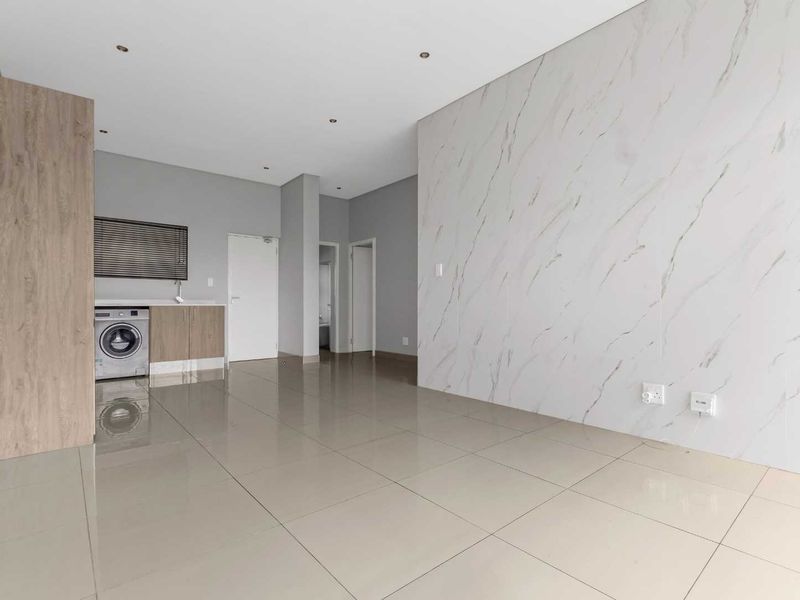 A bright, modern open-plan living area featuring large-format porcelain tiles, a striking marble-effect feature wall, and a discreet built-in laundry nook.
