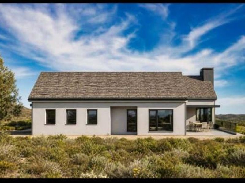 A modern single-story house featuring a pitched roof, clean stucco exterior, and a covered rear patio overlooking a natural landscape.