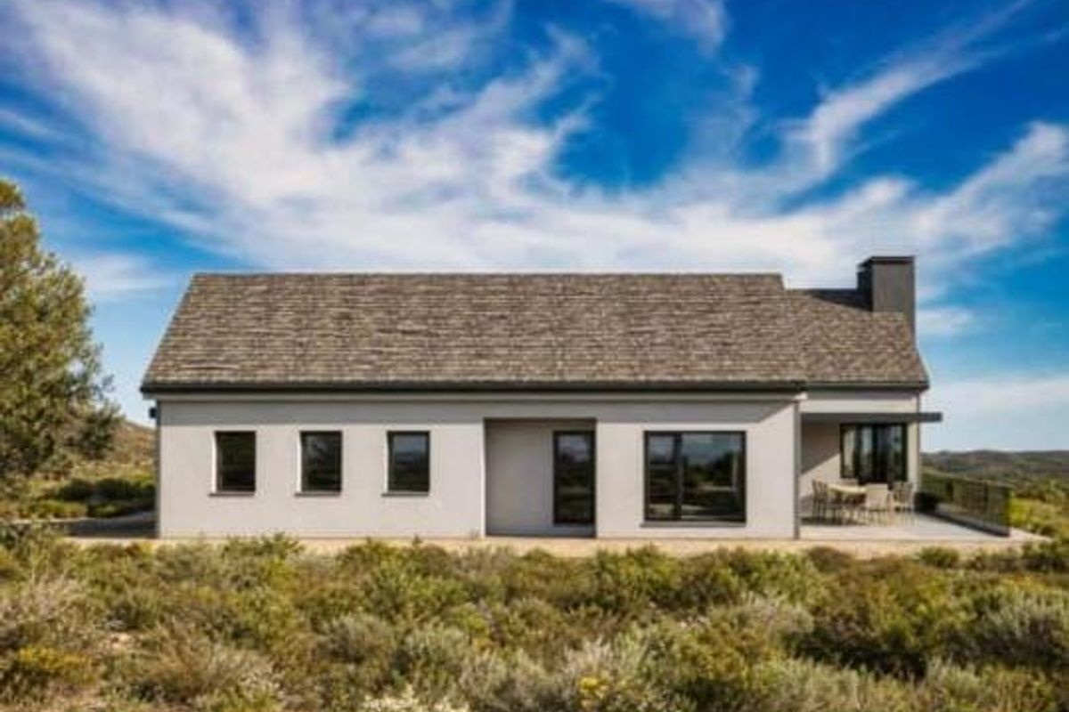 A modern single-story house featuring a pitched roof, clean stucco exterior, and a covered rear patio overlooking a natural landscape.