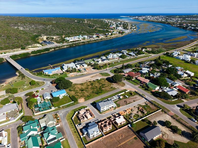 An aerial view of a coastal residential area featuring a river, bridge, and surrounding landscape.