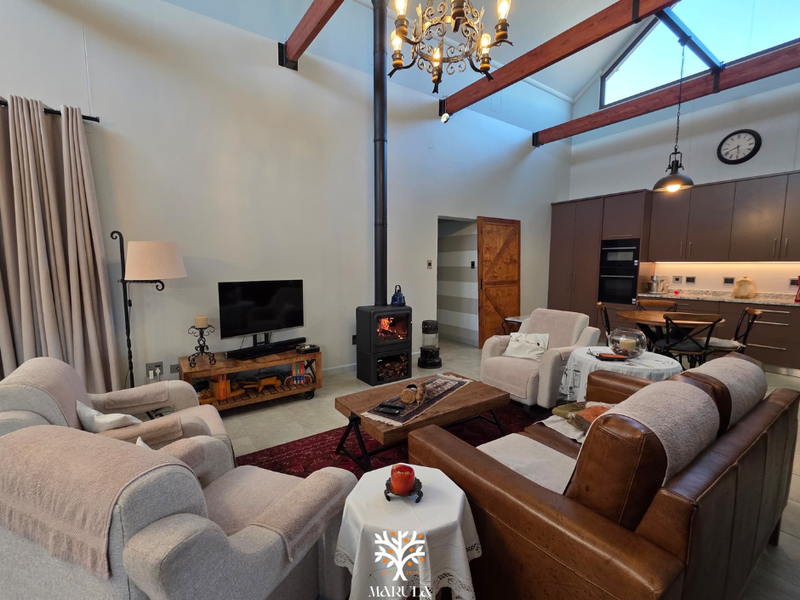 Spacious open-plan living area featuring high vaulted ceilings with exposed timber beams, a modern wood-burning fireplace, and an integrated kitchen with sleek cabinetry.