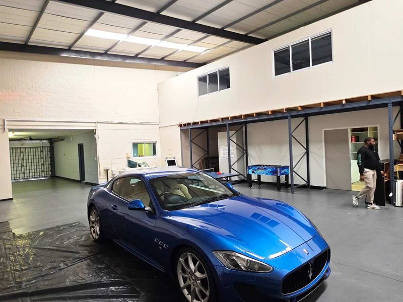 Spacious industrial garage featuring high ceilings with exposed trusses, epoxy flooring, a mezzanine level, and integrated steel storage racking.