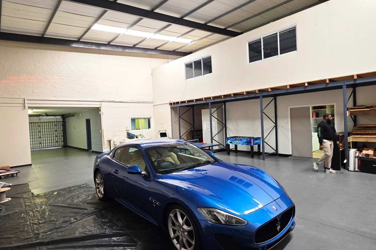 Spacious industrial garage featuring high ceilings with exposed trusses, epoxy flooring, a mezzanine level, and integrated steel storage racking.