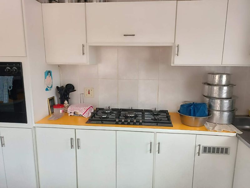 A functional kitchen featuring white cabinetry, a gas hob, built-in oven, and tiled splashback with a yellow laminate countertop.