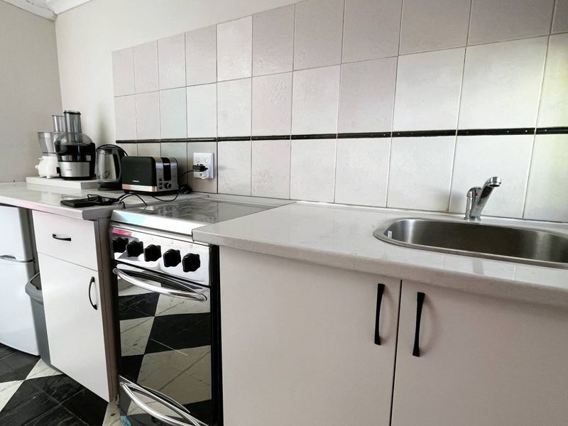 Compact kitchen featuring white cabinetry, tiled backsplash, stainless steel sink, and a freestanding stove with a checkerboard floor finish.