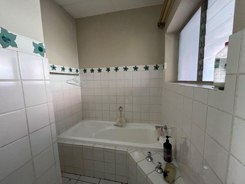 A functional bathroom featuring a built-in bathtub with tiled surround and a louver window, offering a dated aesthetic ready for modernization.