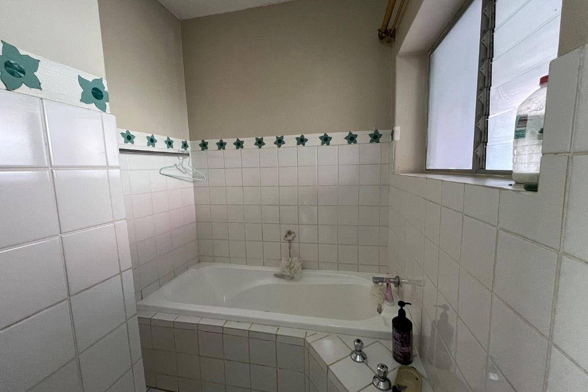 A functional bathroom featuring a built-in bathtub with tiled surround and a louver window, offering a dated aesthetic ready for modernization.