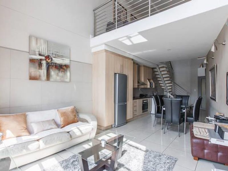 Open-plan living and kitchen area featuring high ceilings, a mezzanine level, modern tiled flooring, and a functional kitchen with built-in cabinetry.