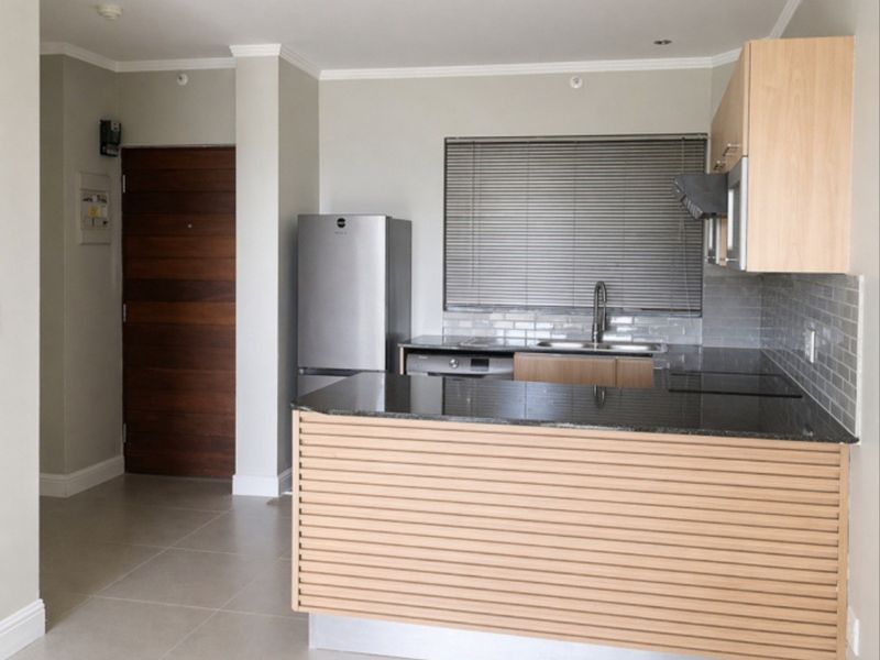 Modern kitchen featuring granite countertops, light wood cabinetry, subway tile backsplash, and integrated stainless steel fixtures in an open-plan layout.