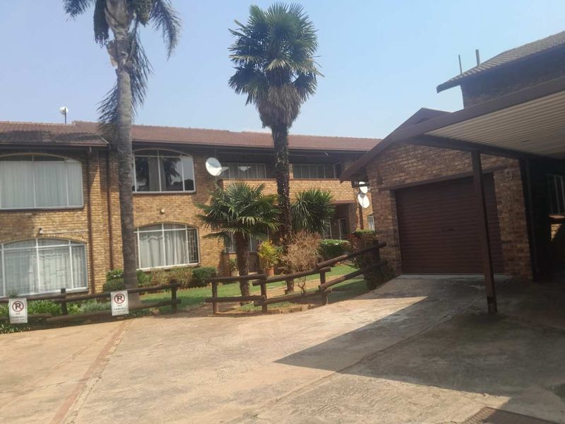Front exterior view of a face brick townhouse complex featuring a concrete driveway, carport, and established garden area.