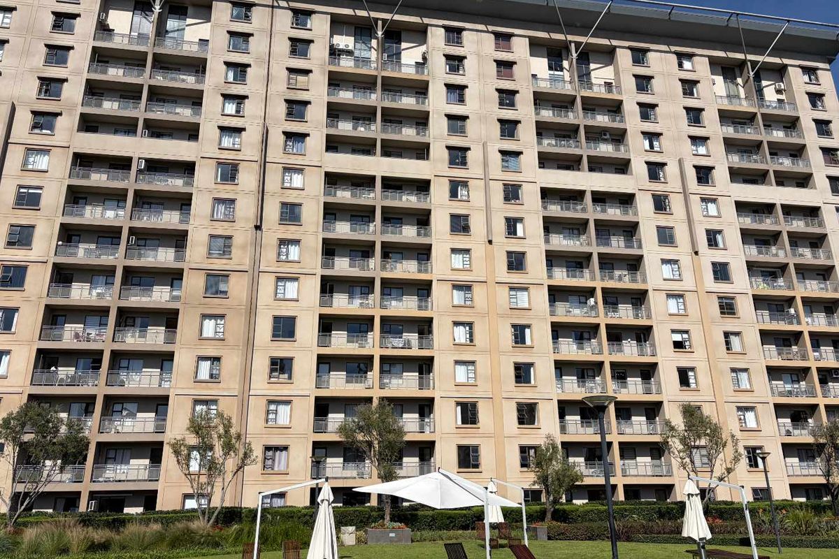 A view of the rear facade of a multi-story apartment complex featuring uniform balconies and a well-maintained communal lawn area.