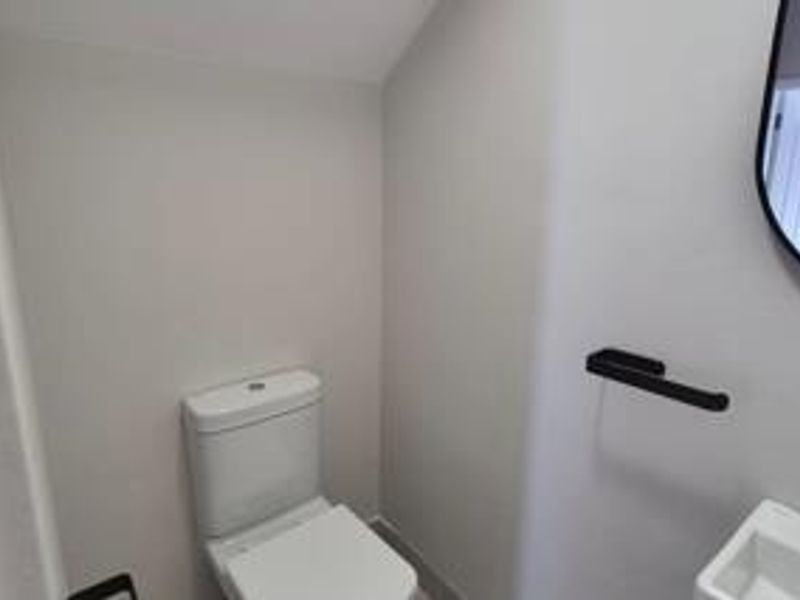 A modern, compact guest bathroom featuring a white toilet, wall-mounted basin, and contemporary black fixtures.