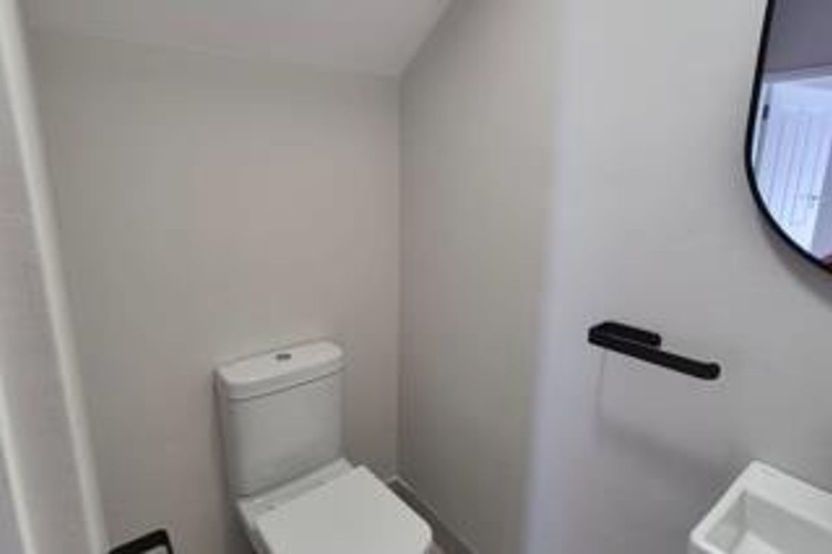 A modern, compact guest bathroom featuring a white toilet, wall-mounted basin, and contemporary black fixtures.