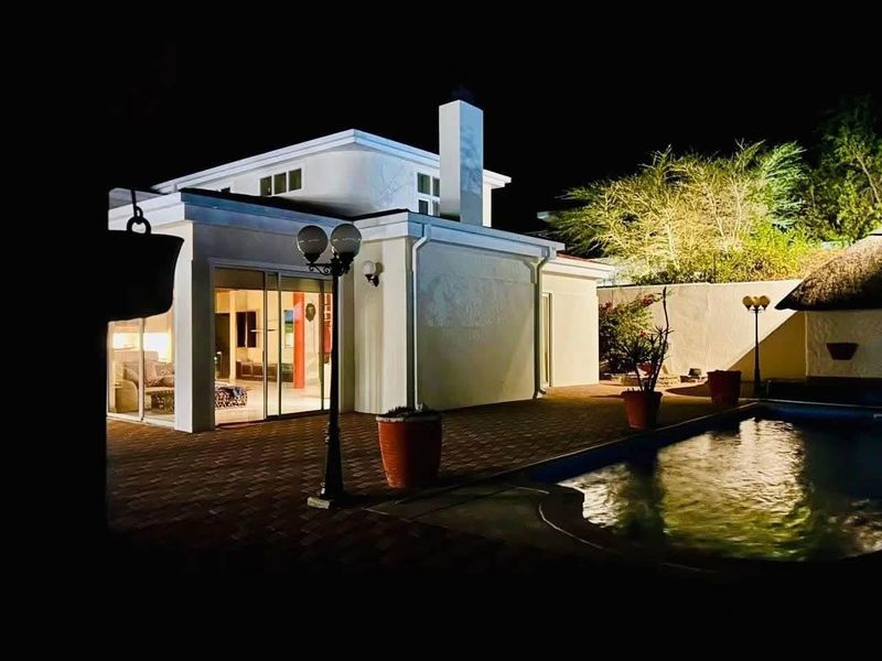 Night view of the rear exterior featuring a paved patio area, swimming pool, and modern building facade with large sliding glass doors.