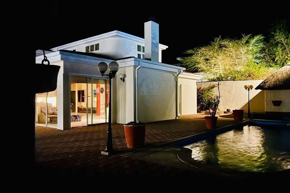 Night view of the rear exterior featuring a paved patio area, swimming pool, and modern building facade with large sliding glass doors.