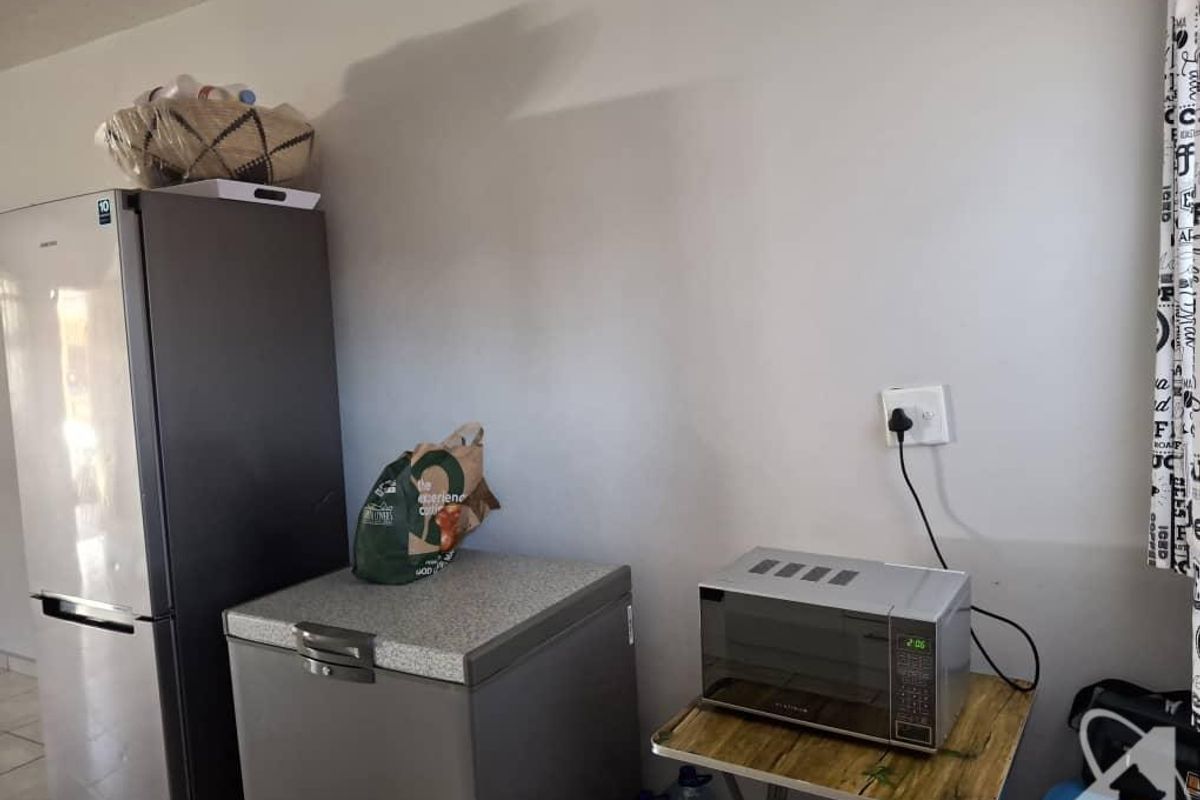 A functional kitchen area featuring a refrigerator, chest freezer, and microwave on a side table with a standard electrical outlet.