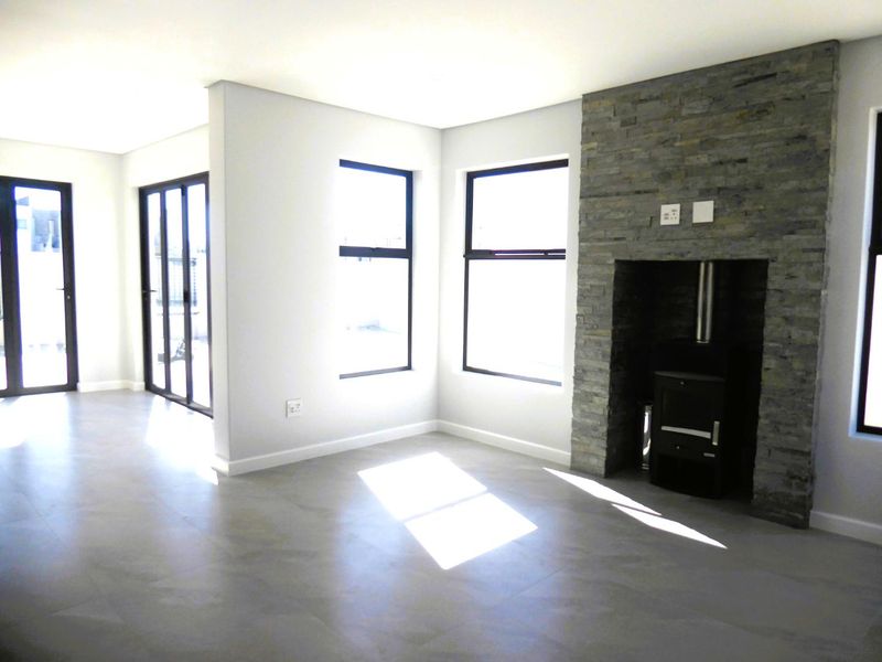 Spacious living area featuring a modern stone-clad fireplace with a wood-burning stove, large windows, and sleek tiled flooring with access to the patio.