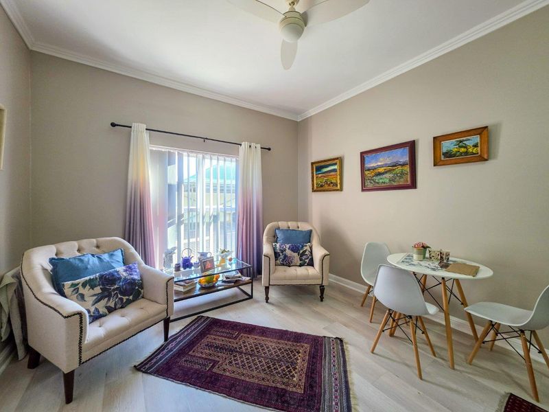 A bright and well-maintained living area featuring neutral wall tones, crown molding, a ceiling fan, and light-toned laminate flooring with access to outdoor space.